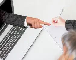 Die Hand eines Mannes zeigt aus einem Laptop heraus.
